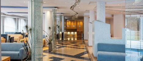 A modern hotel lobby with a check-in area, seating, and a glass partition.