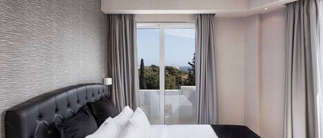 A modern hotel room with a large bed, grey curtains, and a view of the cityscape through large windows.