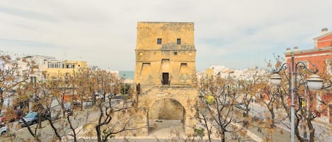 Una torre histórica con un vano central, rodeada de árboles y edificios urbanos.