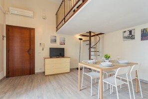 A dining area with a wooden table, white chairs, and a television on a stand. - Casa Torre Lama by Wonderful Italy (Bari)