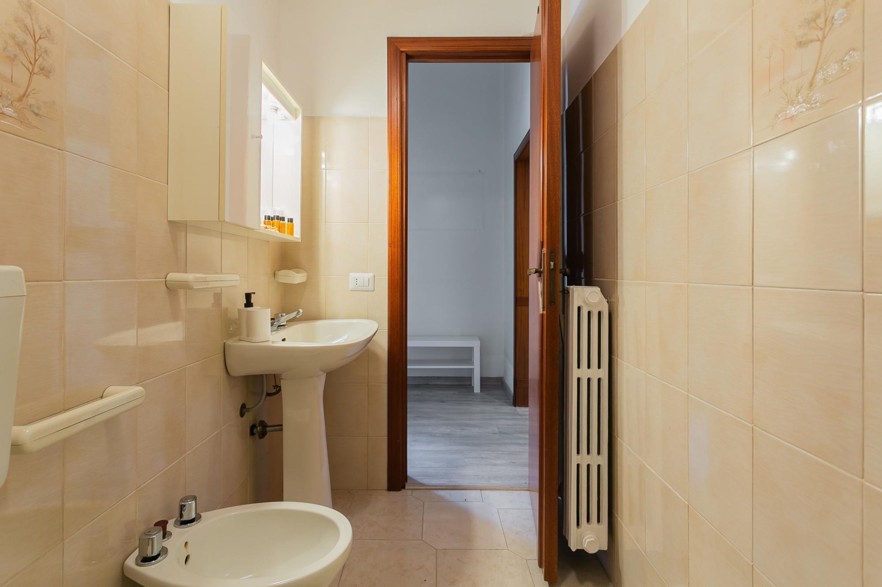 A bathroom with a toilet, sink, and bidet. There is a mirror above the sink and a radiator on the right.
