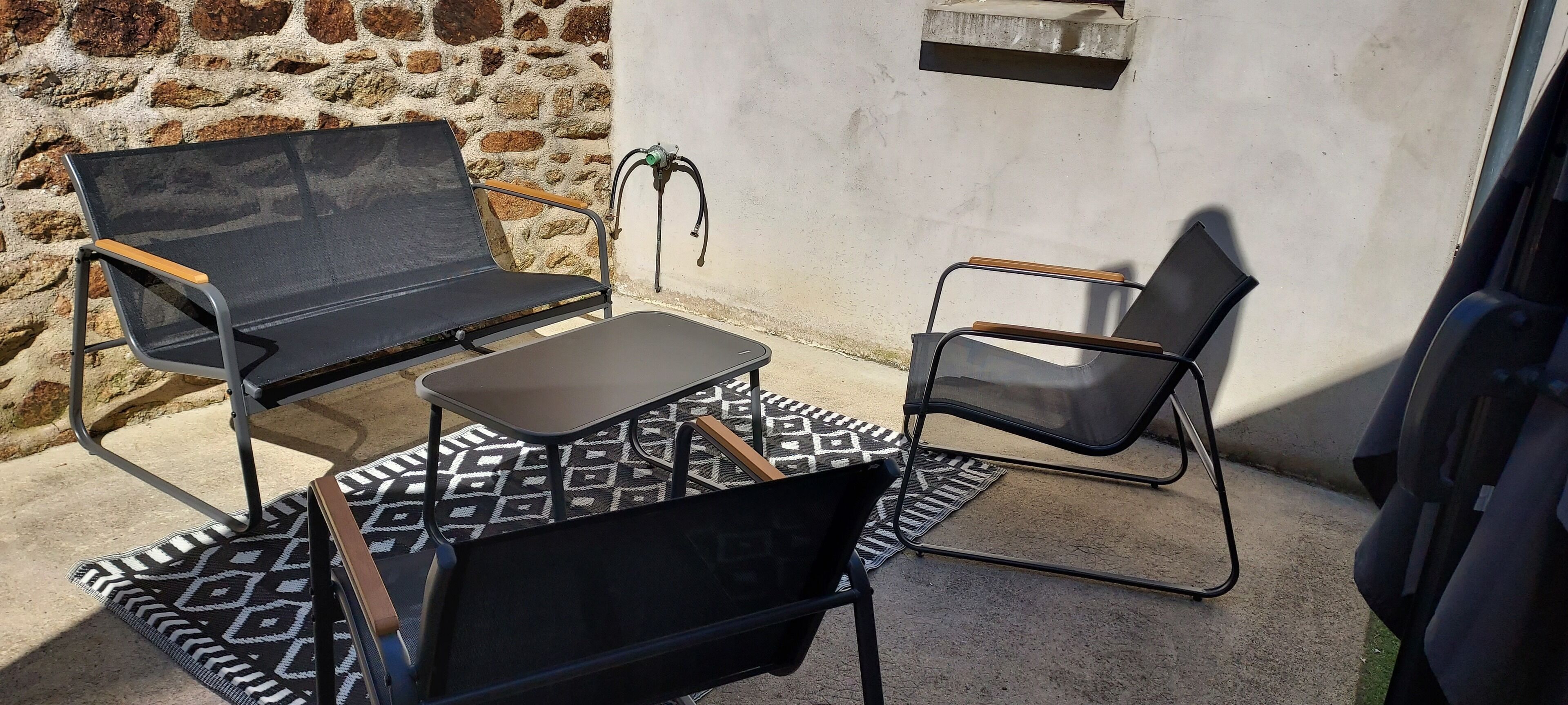 A patio area with two black mesh chairs and a small table, set against a stone wall with a concrete floor.