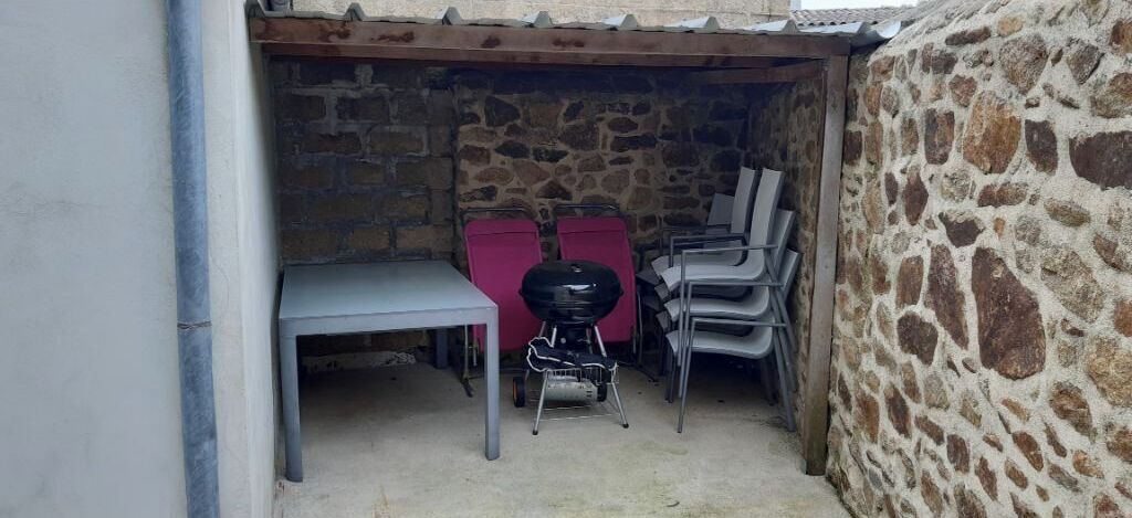 A stone-walled outdoor area with a table and chairs, a barbecue grill, and a small table.