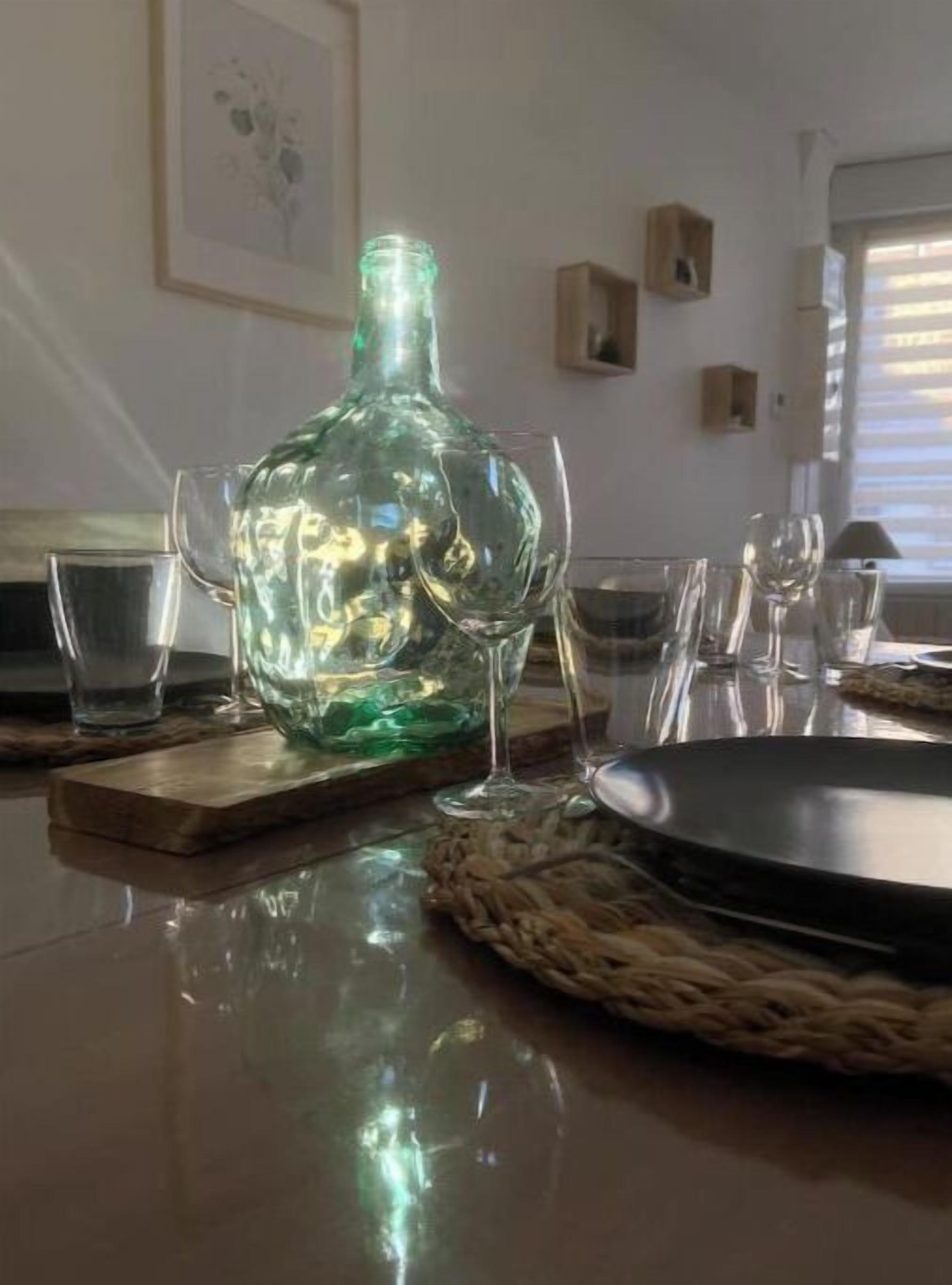 Een eettafel met een groene glazen fles, verschillende wijnglazen en een zwart bord.