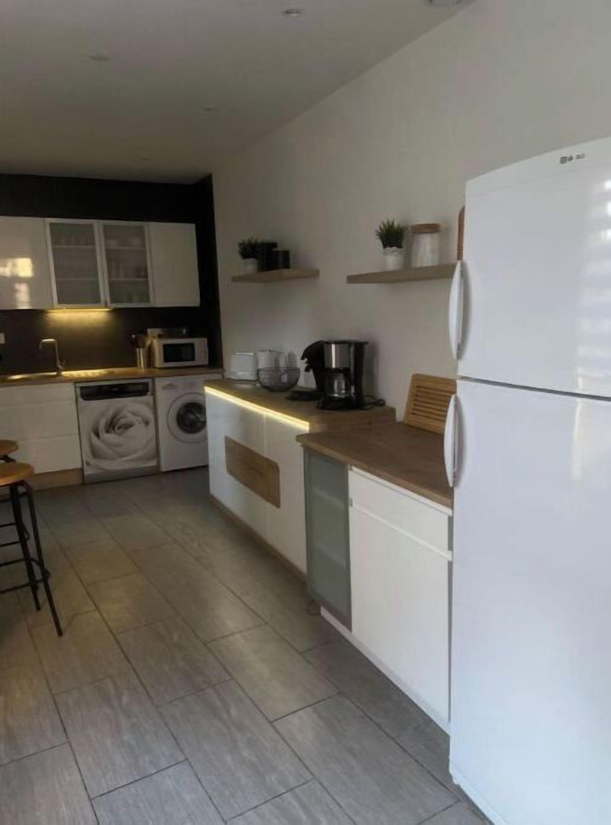 Een moderne keuken met witte kastjes, een ingebouwde wasmachine, een koffiezetapparaat en een koelkast.