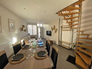 A dining area with a long table set for six, surrounded by chairs. A wooden spiral staircase is visible to the right. - Ducey : Meublé de Tourisme Classé 3 Étoiles (Ducey-les-Chéris)