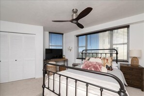 A bedroom with a bed, a ceiling fan, a TV, a desk, and a window with blinds. - Luxury at its Finest - 3306 Towers - Traffic Free Beach - 3/3 Oceanfront (Ponce Inlet)