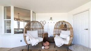 Een kamer met twee rieten stoelen, een bankje en een kleine pompoen decoratie op de vloer.