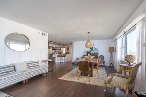 A modern living room with a sofa, dining table, and chairs. There is a kitchen area in the background. - Luxury at its Finest - 3306 Towers - Traffic Free Beach - 3/3 Oceanfront (Ponce Inlet)