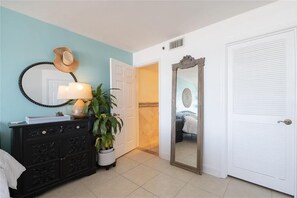 A room with a black dresser, a mirror, a hat on the wall, a potted plant, and a white door.