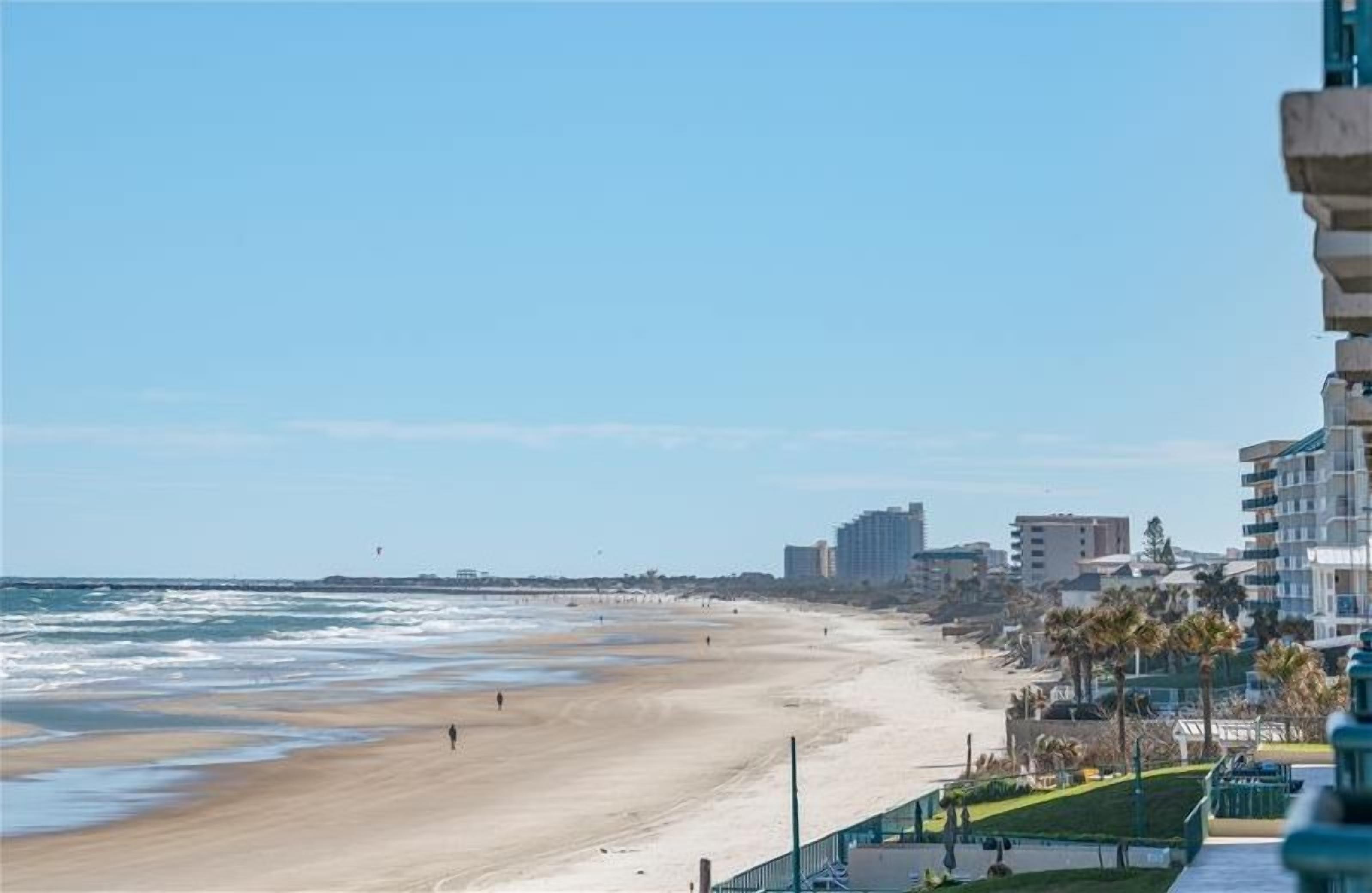 Une plage avec un ciel dégagé, un rivage sablonneux et des bâtiments en arrière-plan.