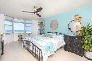 A bedroom with a bed, a ceiling fan, a window with a view, a bedside table, a dresser, and a plant. - Luxury at its Finest - 3306 Towers - Traffic Free Beach - 3/3 Oceanfront (Ponce Inlet)