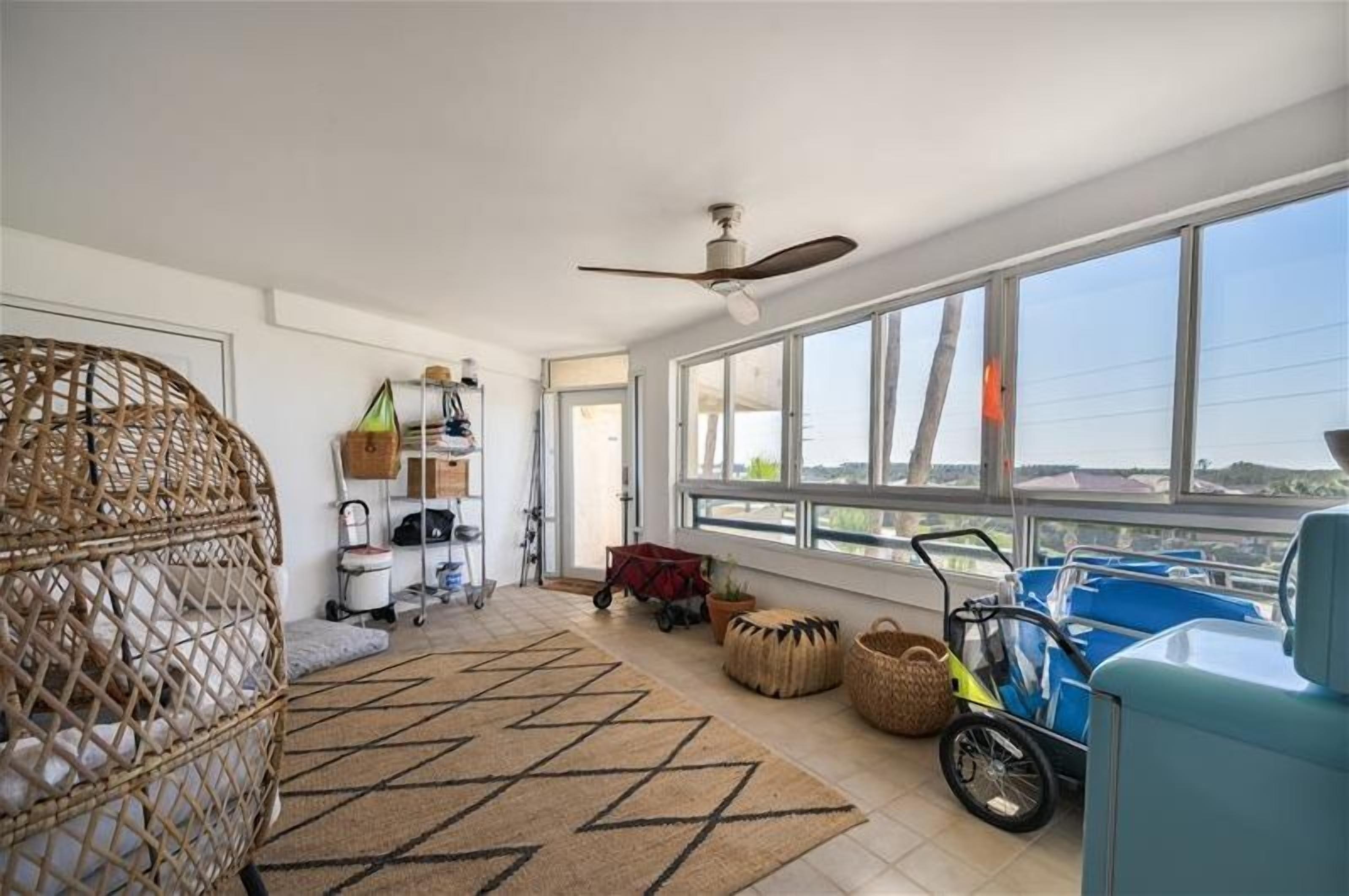 A spacious room with a large window, a ceiling fan, and a wicker chair.