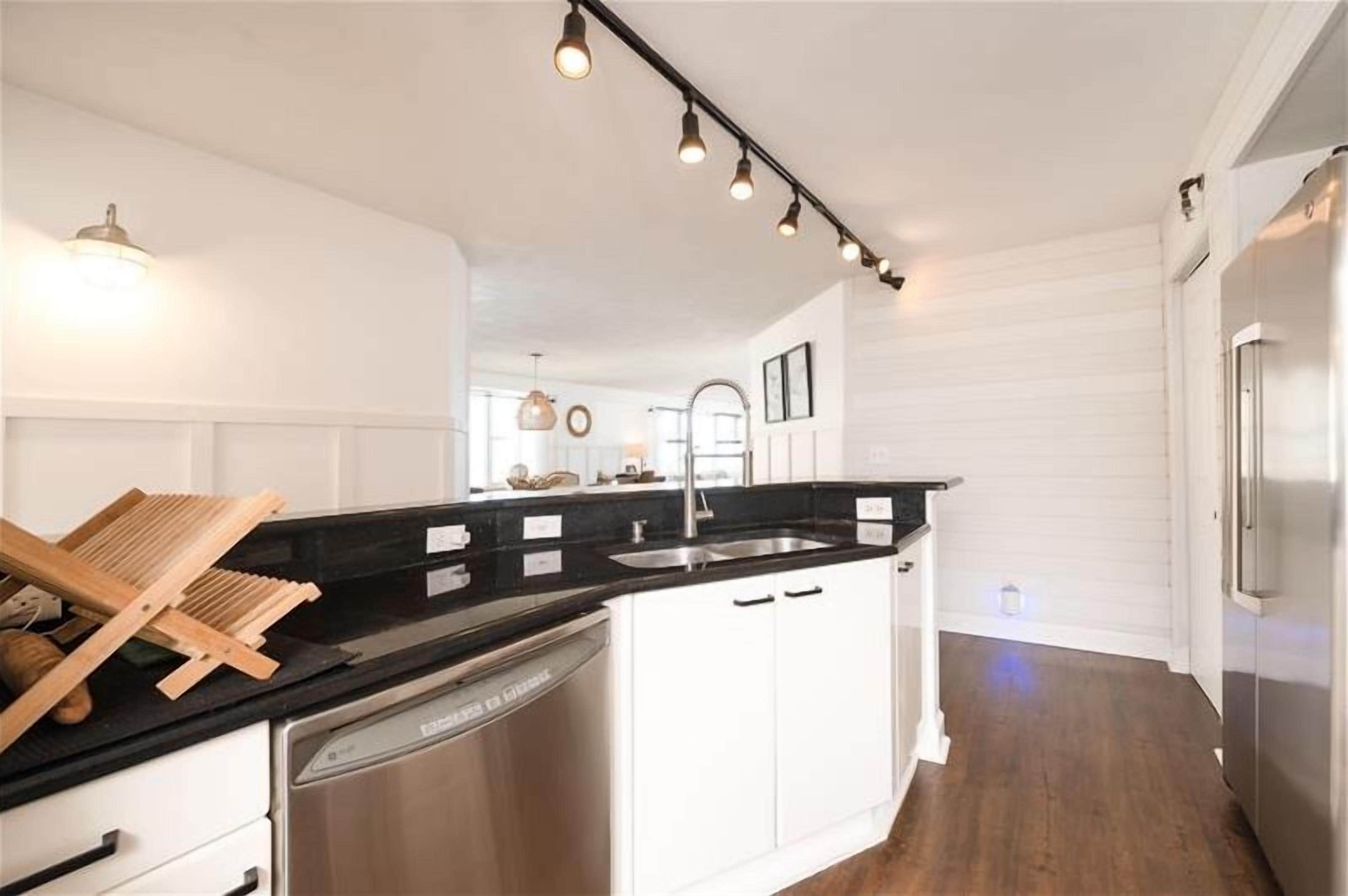 A modern kitchen with white cabinetry, a black countertop, stainless steel appliances, and pendant lighting.
