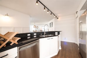 A modern kitchen with white cabinetry, a black countertop, stainless steel appliances, and pendant lighting.