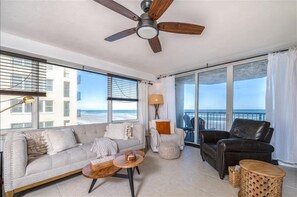 A spacious living room with a large window offering a view of the ocean, a ceiling fan, and a balcony with a view. - Luxury at its Finest - 3306 Towers - Traffic Free Beach - 3/3 Oceanfront (Ponce Inlet)
