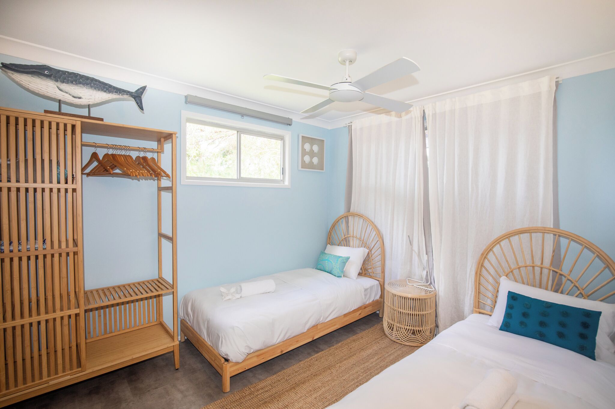 Quarto com uma cama de solteiro, um guarda-roupa de madeira, um ventilador de teto e uma janela com cortinas.