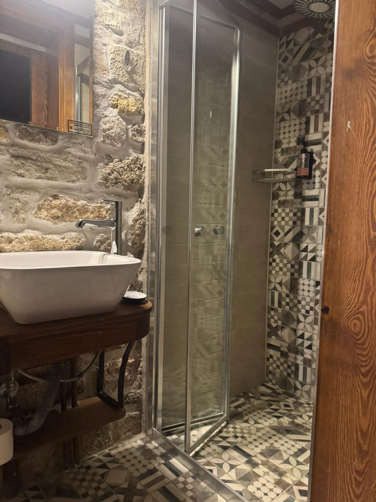 Un baño con pared de piedra, cabina de ducha de vidrio y lavabo.