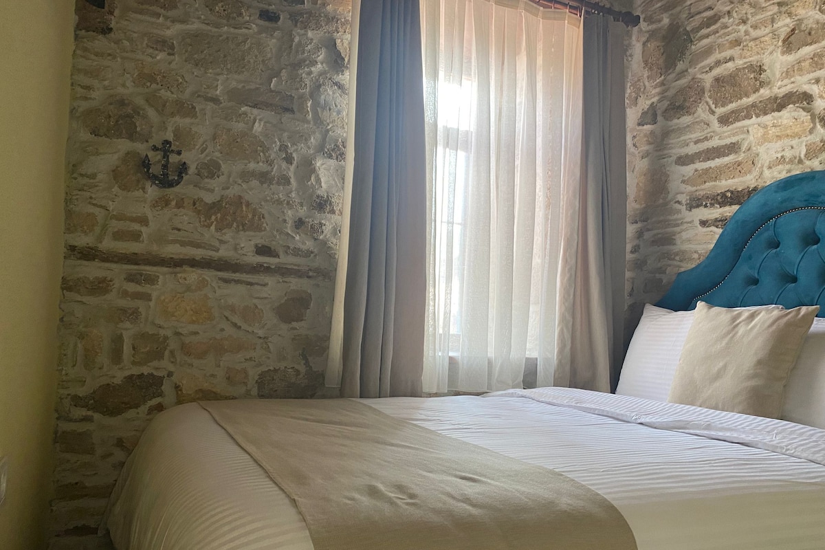 A room with a stone wall, a bed with white bedding, and a blue headboard.