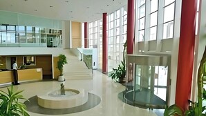 A spacious lobby with a central staircase, a reception desk, and potted plants.