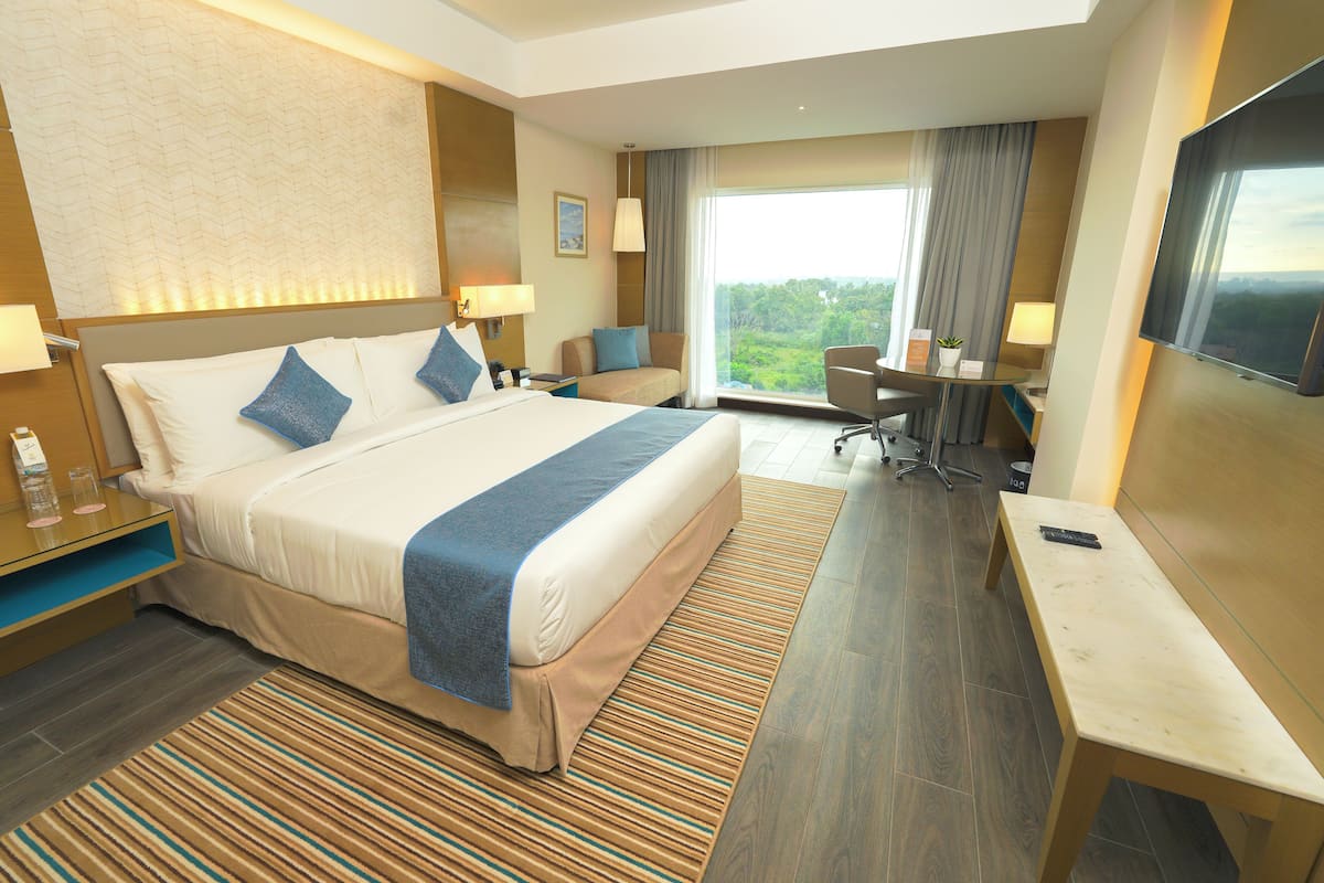 Ein Hotelzimmer mit einem großen Bett, einem Schreibtisch, einem Sessel und einem Fernseher.