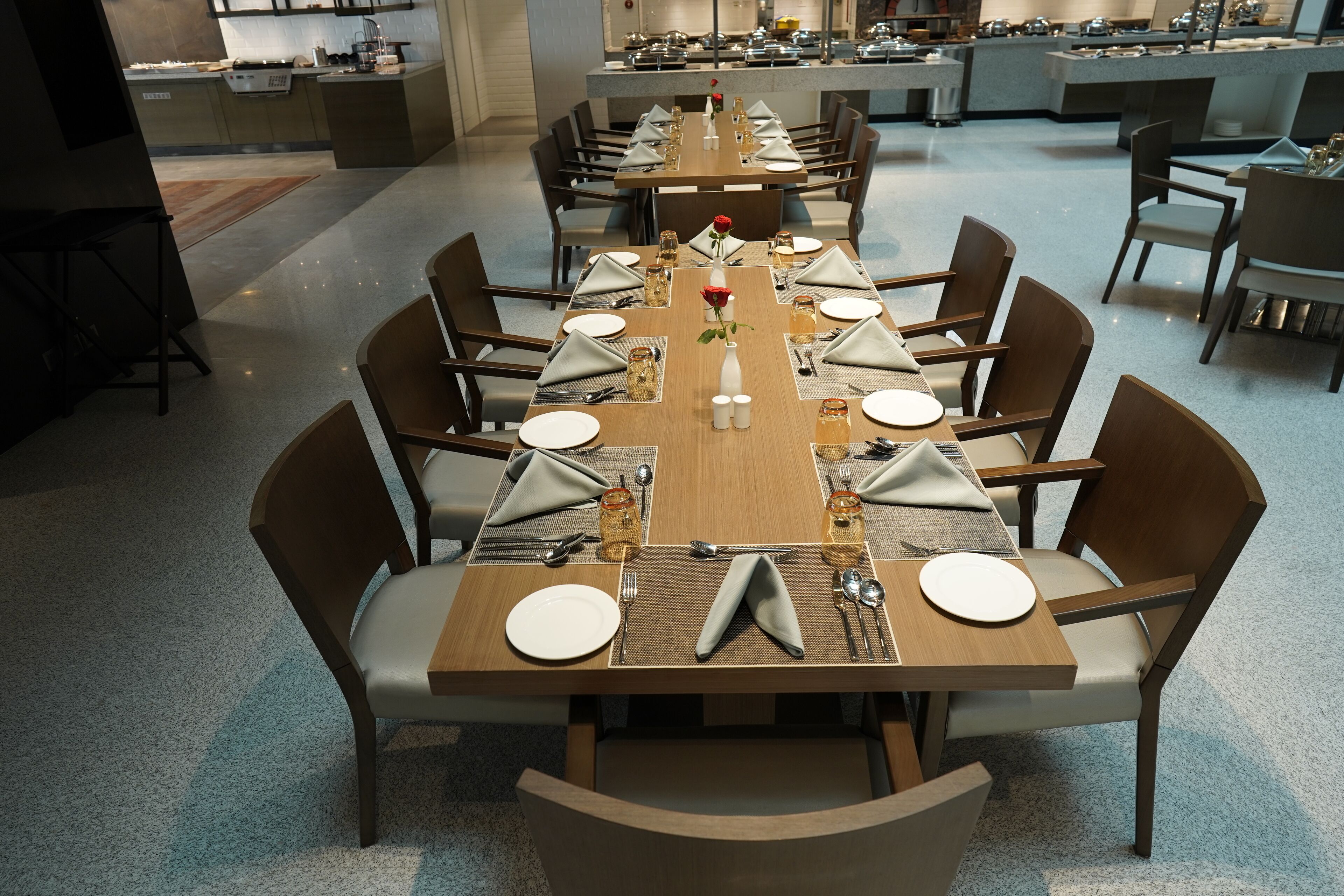 Een lange eettafel gedekt voor een formeel diner, met meerdere stoelen, een vaas met een rode roos en diverse bestek.