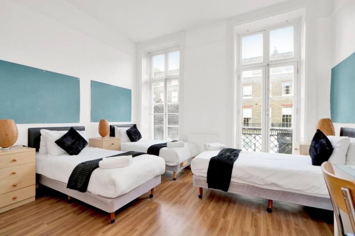 Habitación de hotel moderna con dos camas individuales, un escritorio pequeño, una silla y un ventanal grande con vistas a la ciudad.