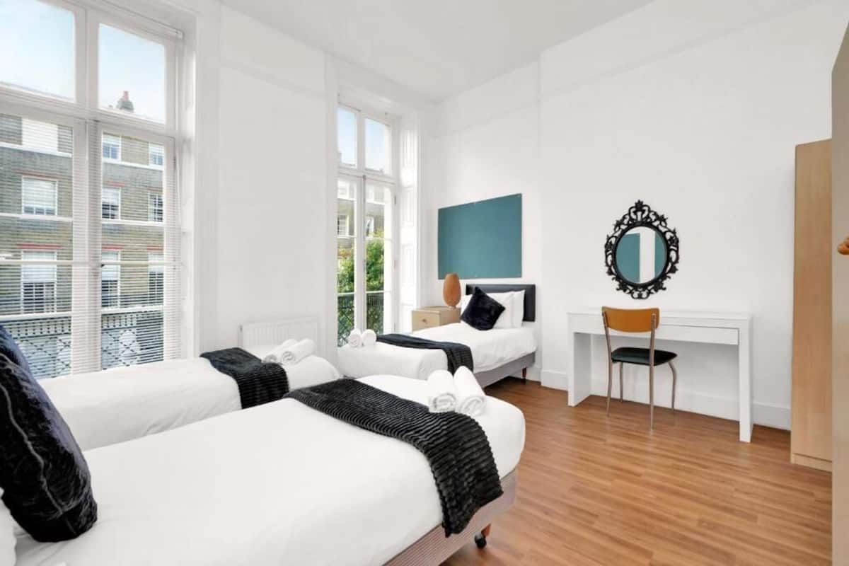Habitación de hotel con dos camas, un escritorio, una silla y un ventanal grande.