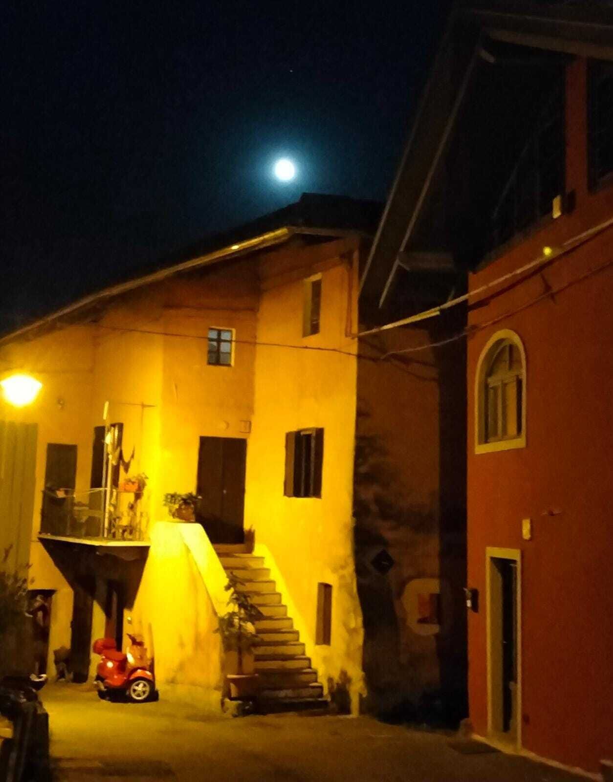 A building with a staircase leading to a balcony, a small red car parked in front, and a bright light source to the left.