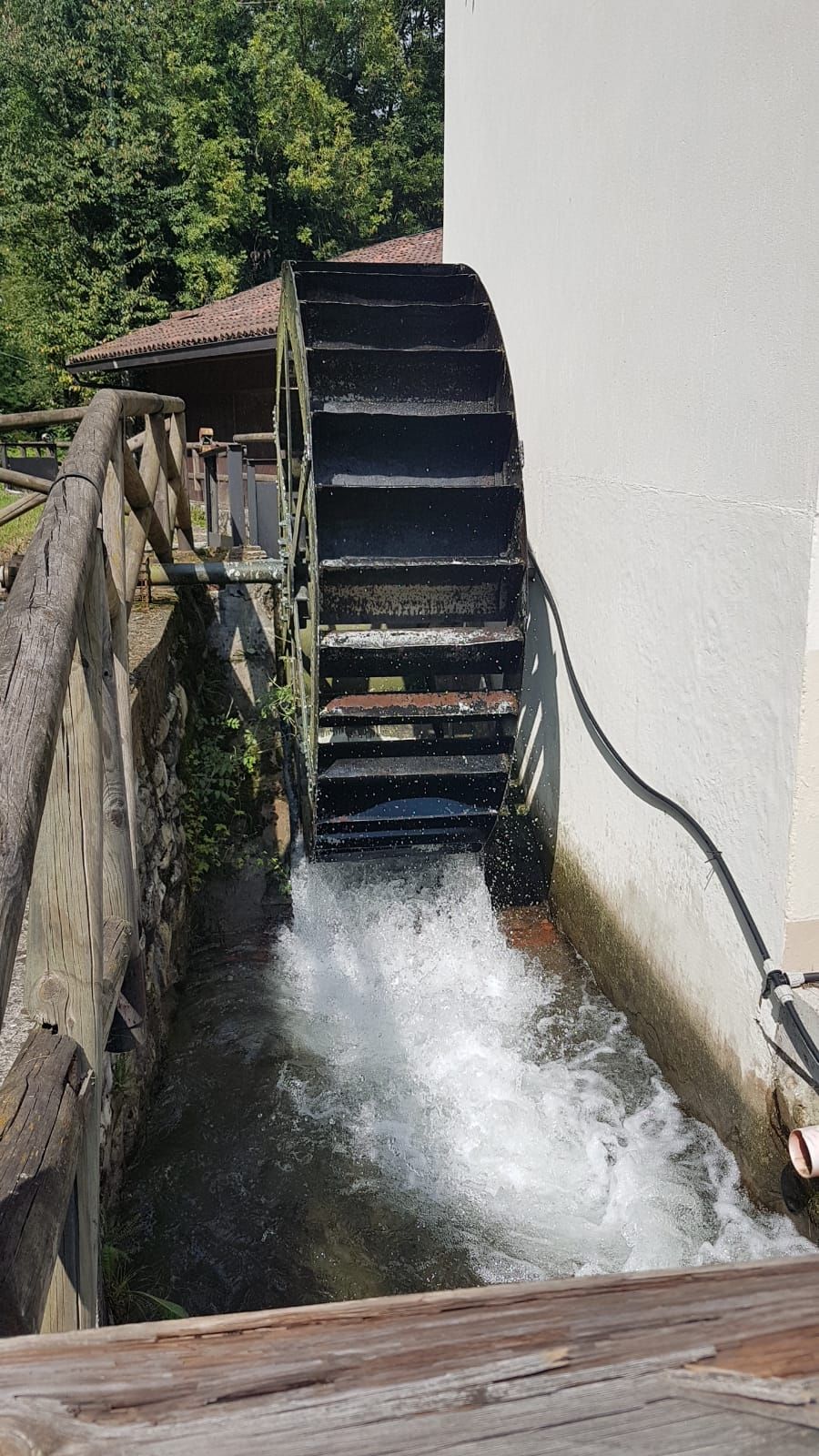 A water wheel with water flowing through it, connected to a wooden structure.