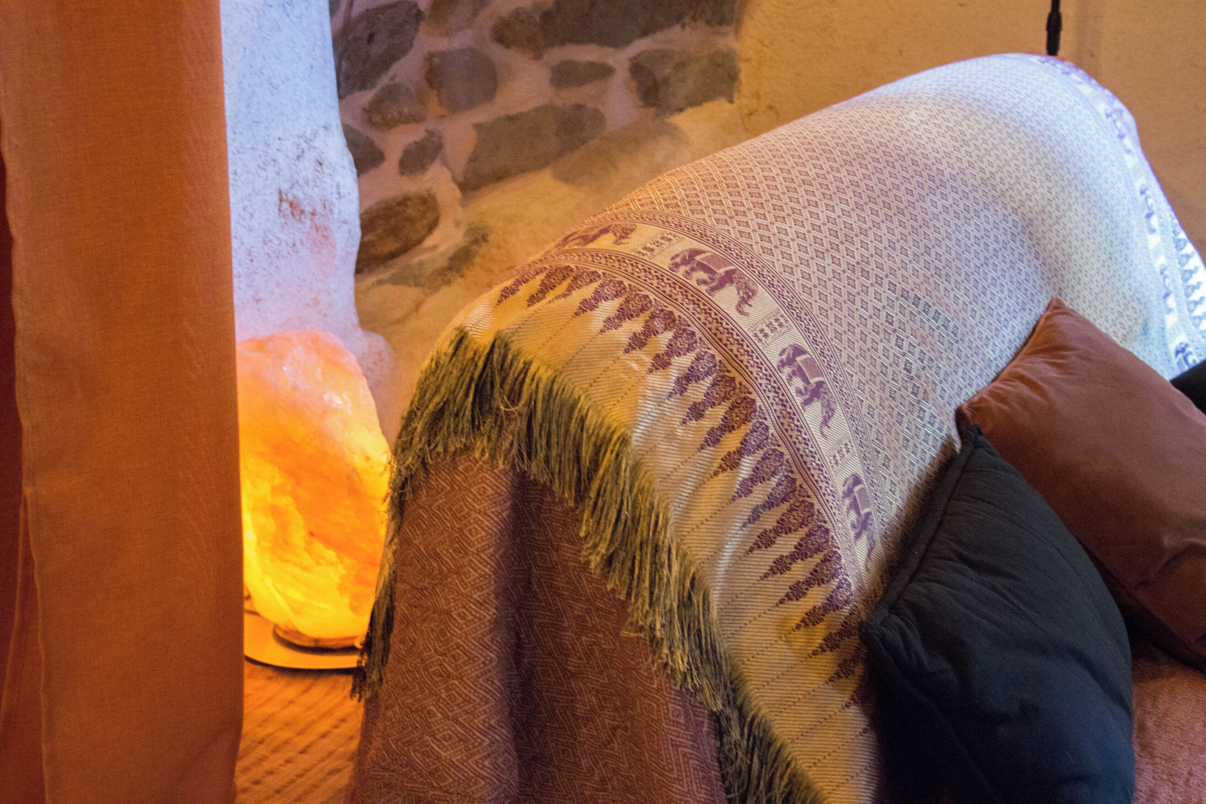 A room with a stone wall, a textured blanket, and a lit lamp.