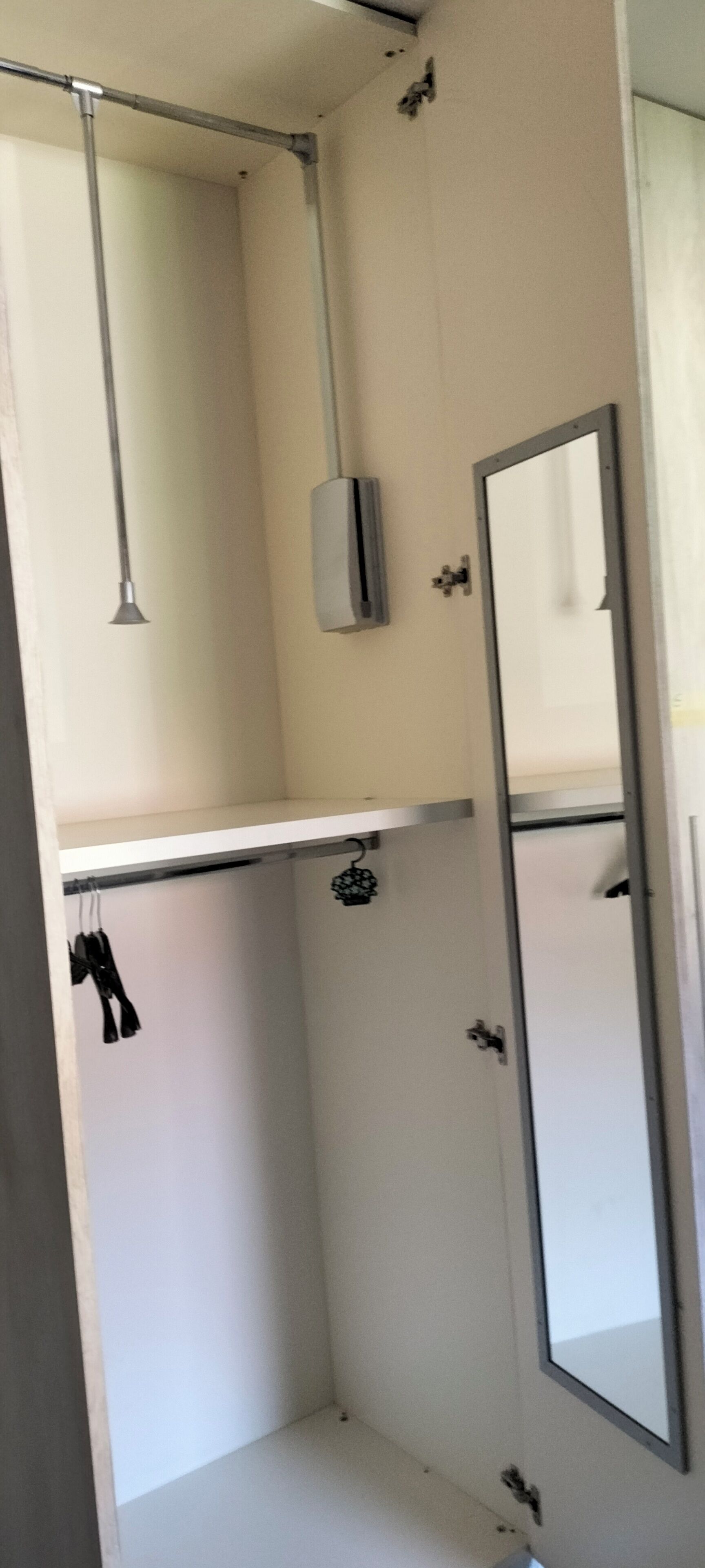 A room with a white wardrobe, a hanging light fixture, and a mirror on the wall.