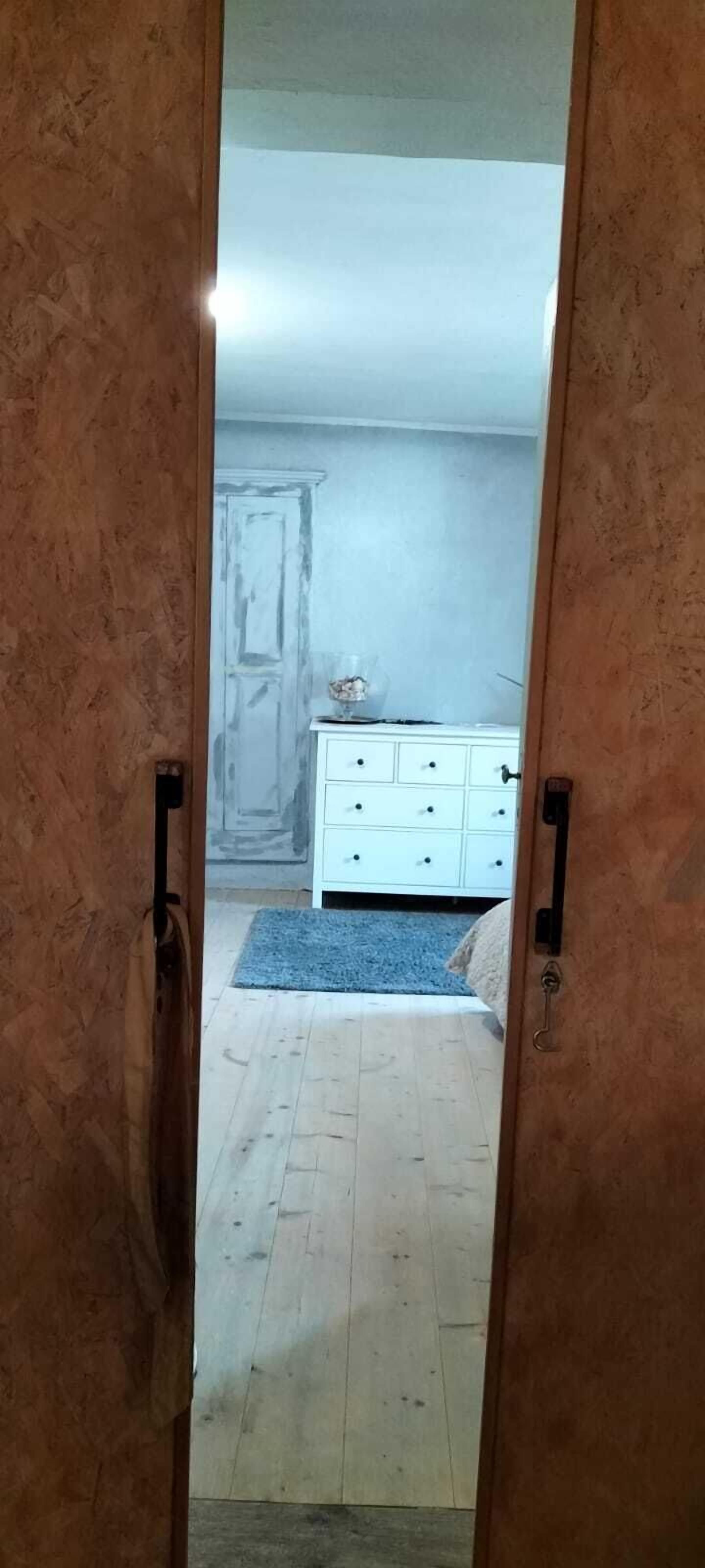 A room with a wooden floor, a white dresser, and a blue rug.