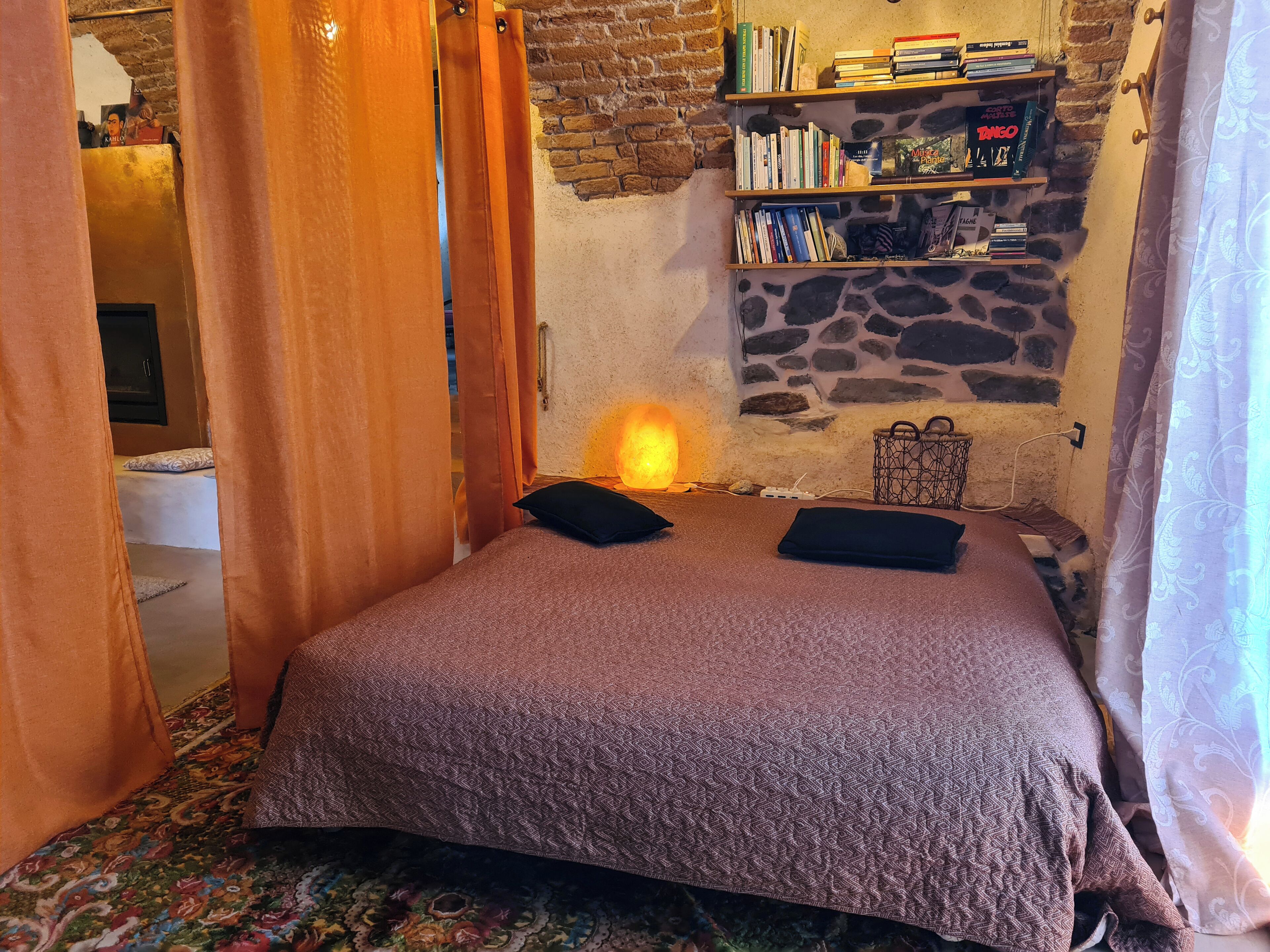 Une pièce chaleureuse avec un lit, un mur en pierre, une bibliothèque et un fauteuil de massage.