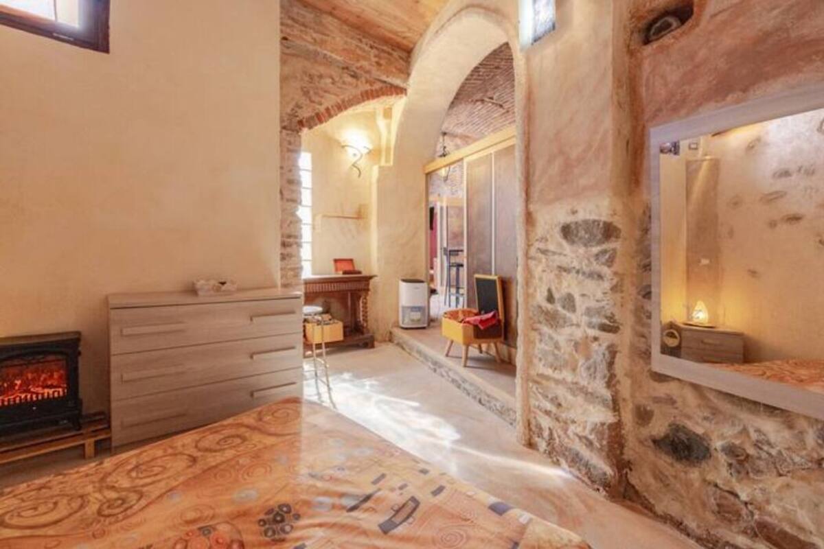 Une pièce avec une cheminée, une commode en bois, un tapis à motifs et des murs en pierre.