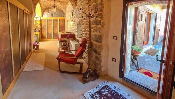 A cozy room with a stone wall, a red chair, a table with a white tablecloth, and a view of the street outside. - CasaRosada Wellness Guest House (Vidracco)