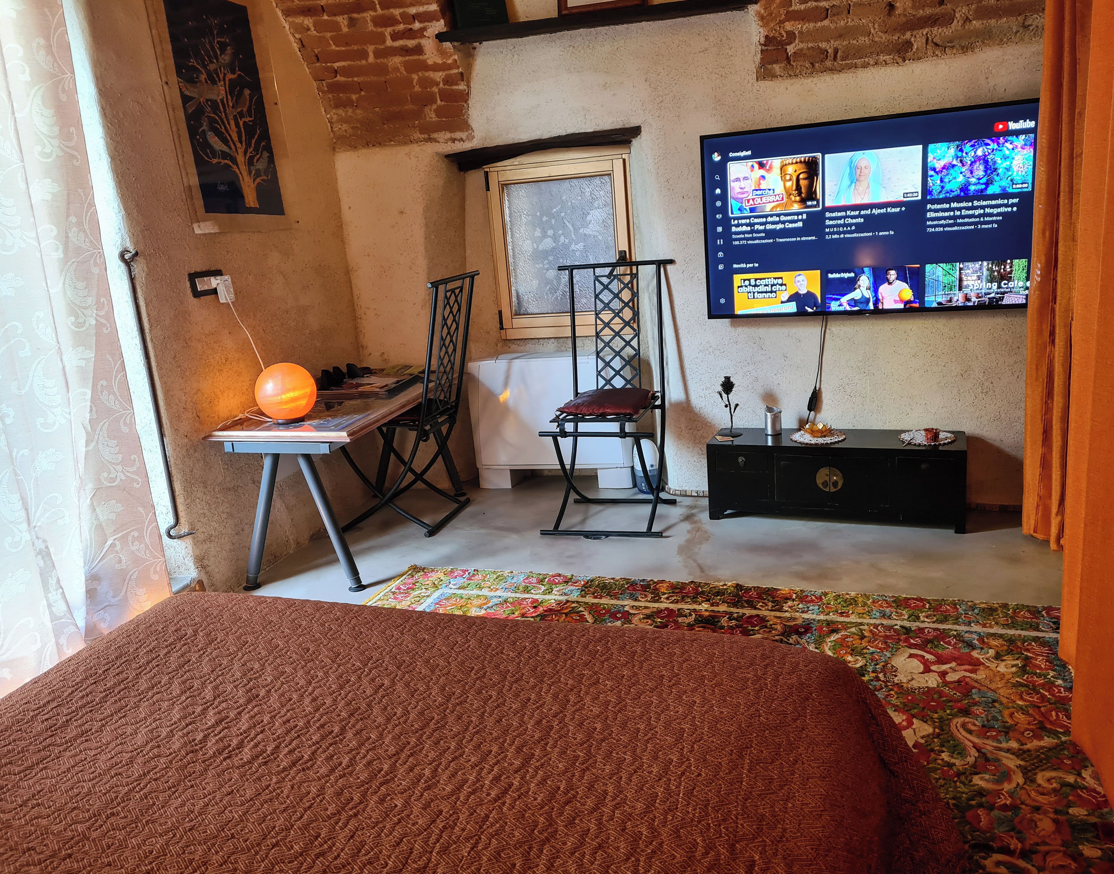 Een kamer met een bed, een bureau met lamp, een stoel, een televisie en een raam.