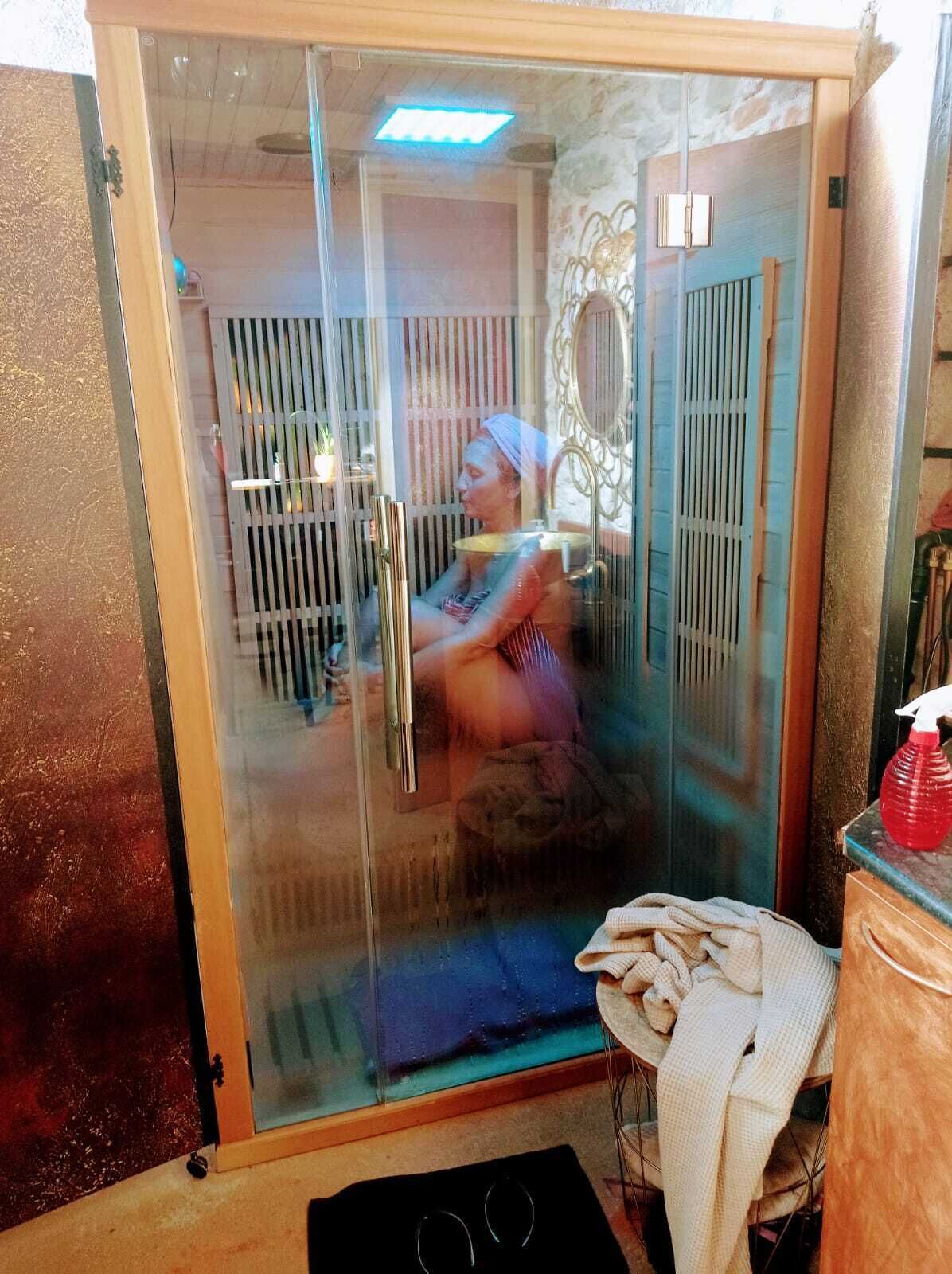 A glass-enclosed room with a shower, a towel, and a bottle of red liquid on a counter.