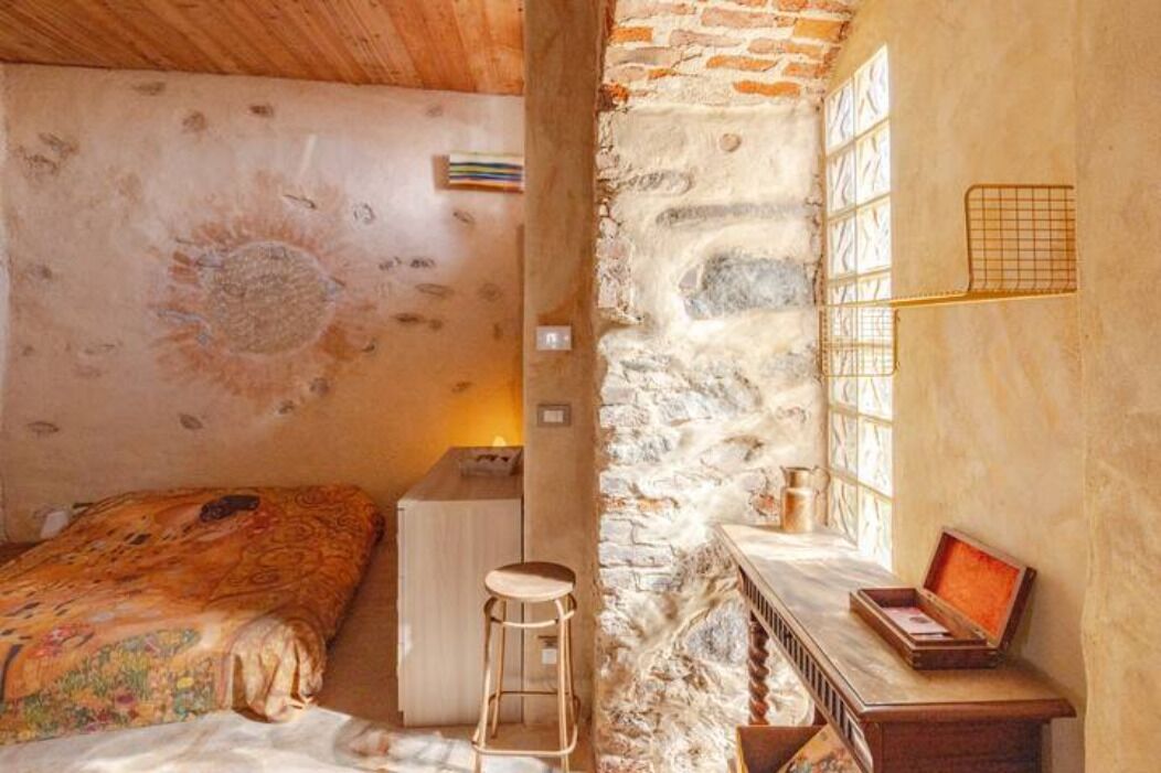 A cozy room with a bed, a small desk, and a stone wall.