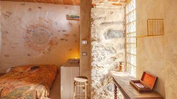 A cozy room with a bed, a small desk, and a stone wall.
