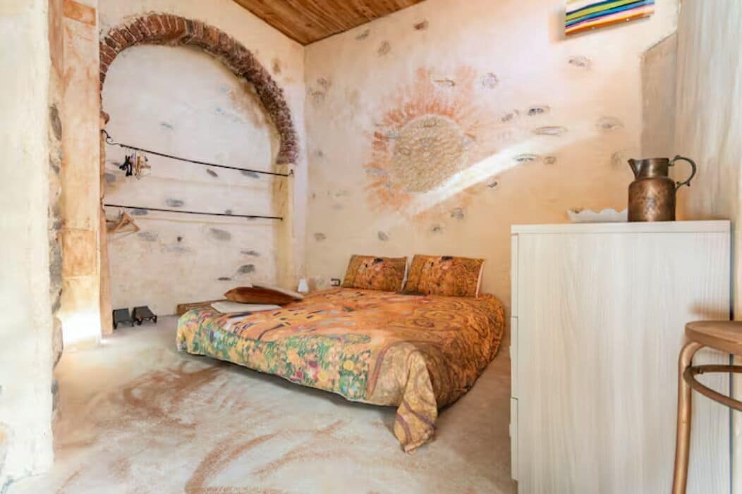 Un dormitorio con cama, un banco de madera, un armario y un mural decorativo en la pared.