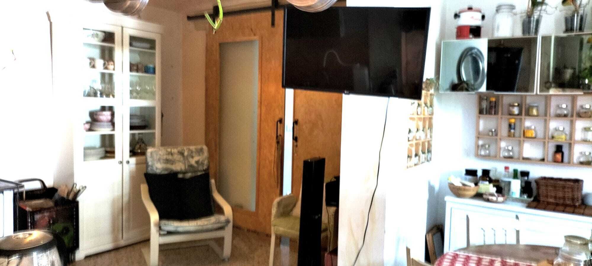 Een kamer met een televisie, een stoel, een kast met glazen deuren en een plank met potten.