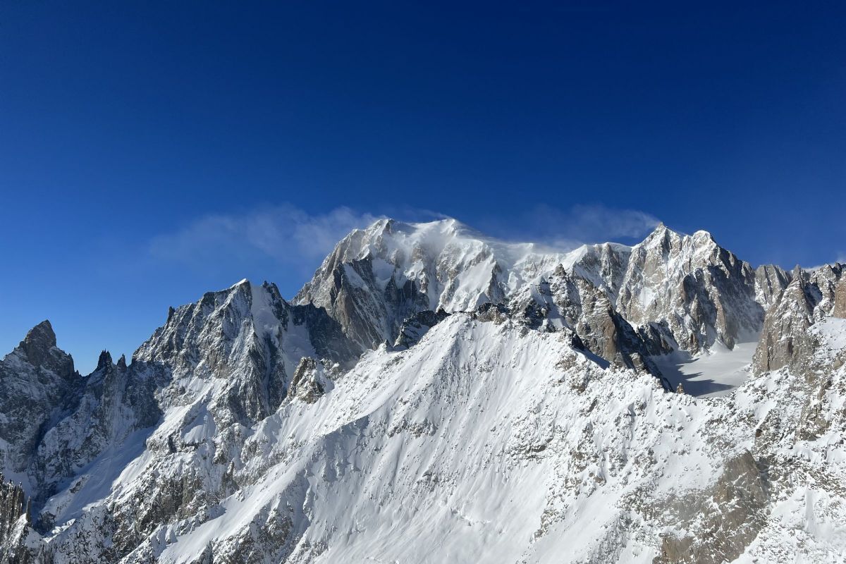 A snow-covered mountain peak with sharp, rugged terrain and a clear blue sky.