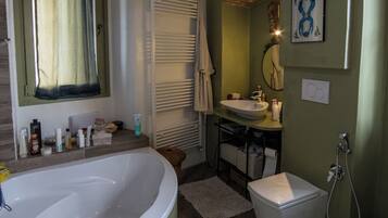 Un baño con bañera, lavamanos e inodoro. Cuenta con una ventana con cortinas, un perchero para toallas y una lámpara colgante.