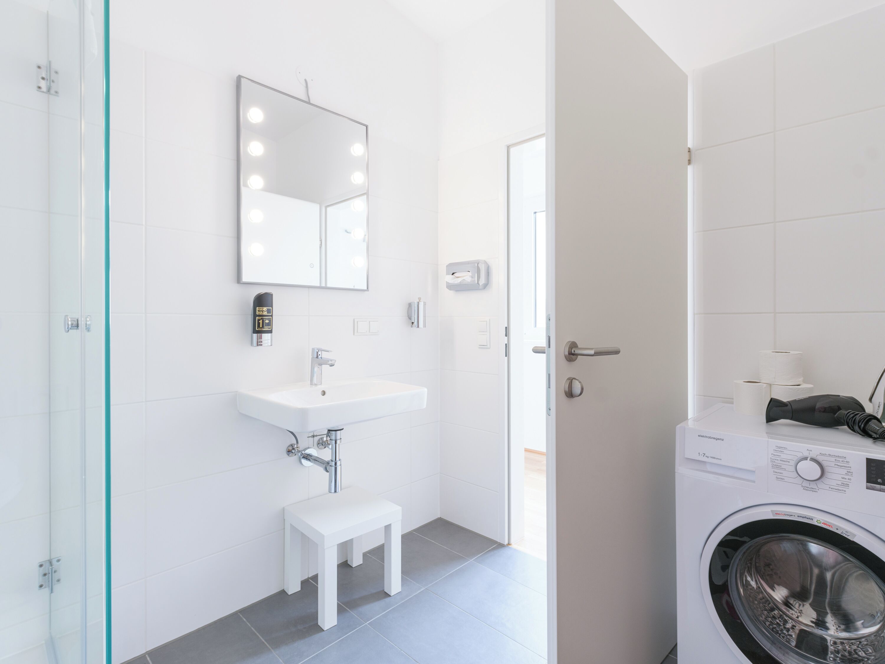 A modern bathroom with a sink, mirror, and a washing machine.