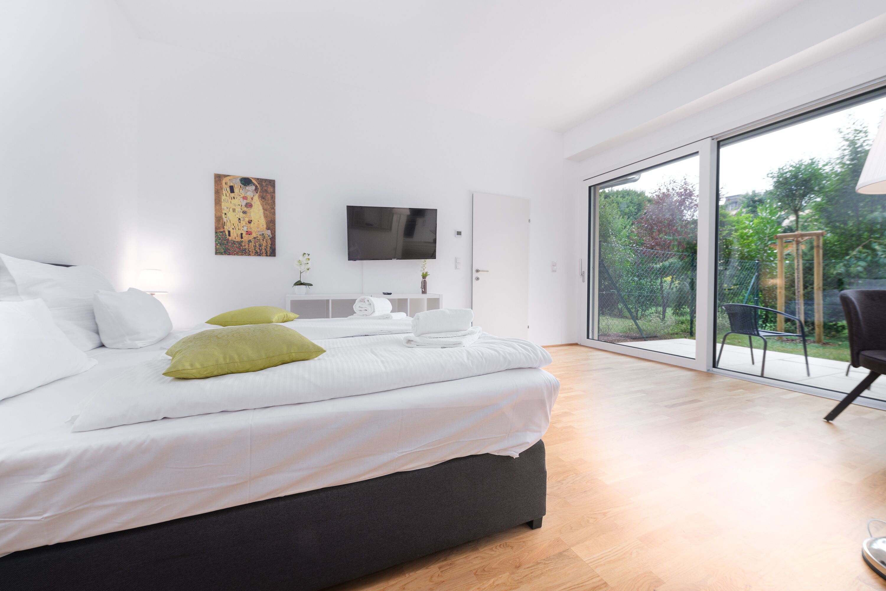 Une chambre moderne dotée d’un grand lit, d’un téléviseur à écran plat et d’une porte-fenêtre coulissante donnant sur un balcon.