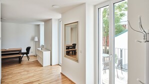 A spacious room with a wooden floor, a desk, a chair, a large mirror, and a sliding glass door leading to an outdoor area with a table and chairs. - My Schönbrunn Apartments (Vienna)