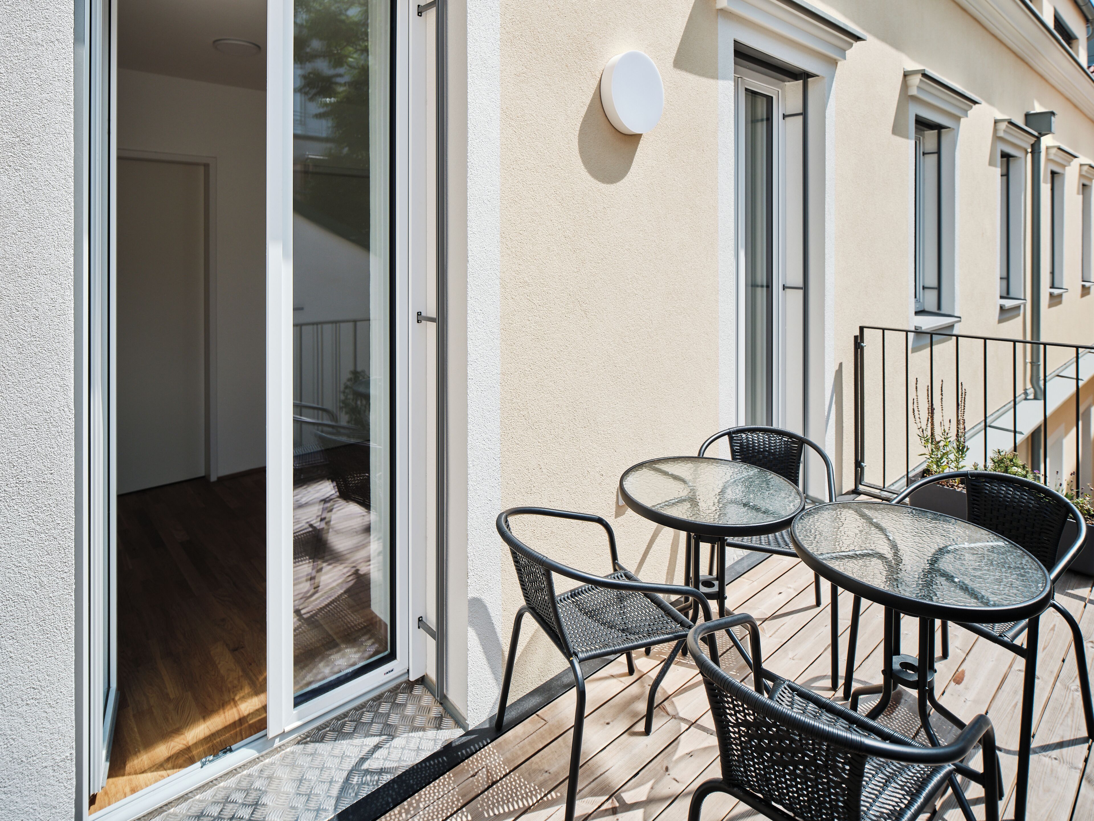 Eine Außenpatio mit Glastür zu einem Innenraum, einem kleinen Tisch mit Stühlen und einem Blumentopf.