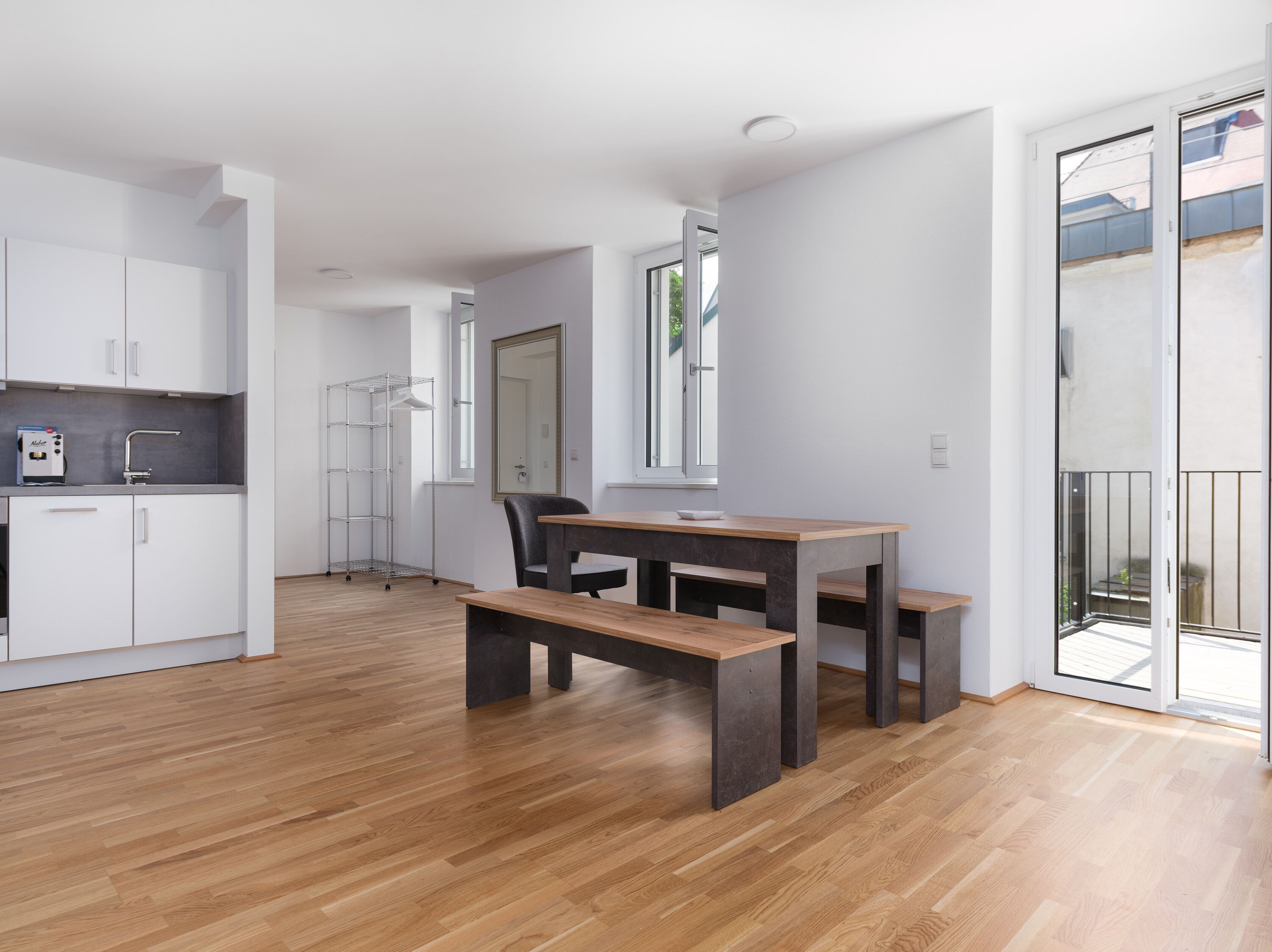 A modern kitchen with white cabinets, a stainless steel range hood, and a wooden dining table with benches.