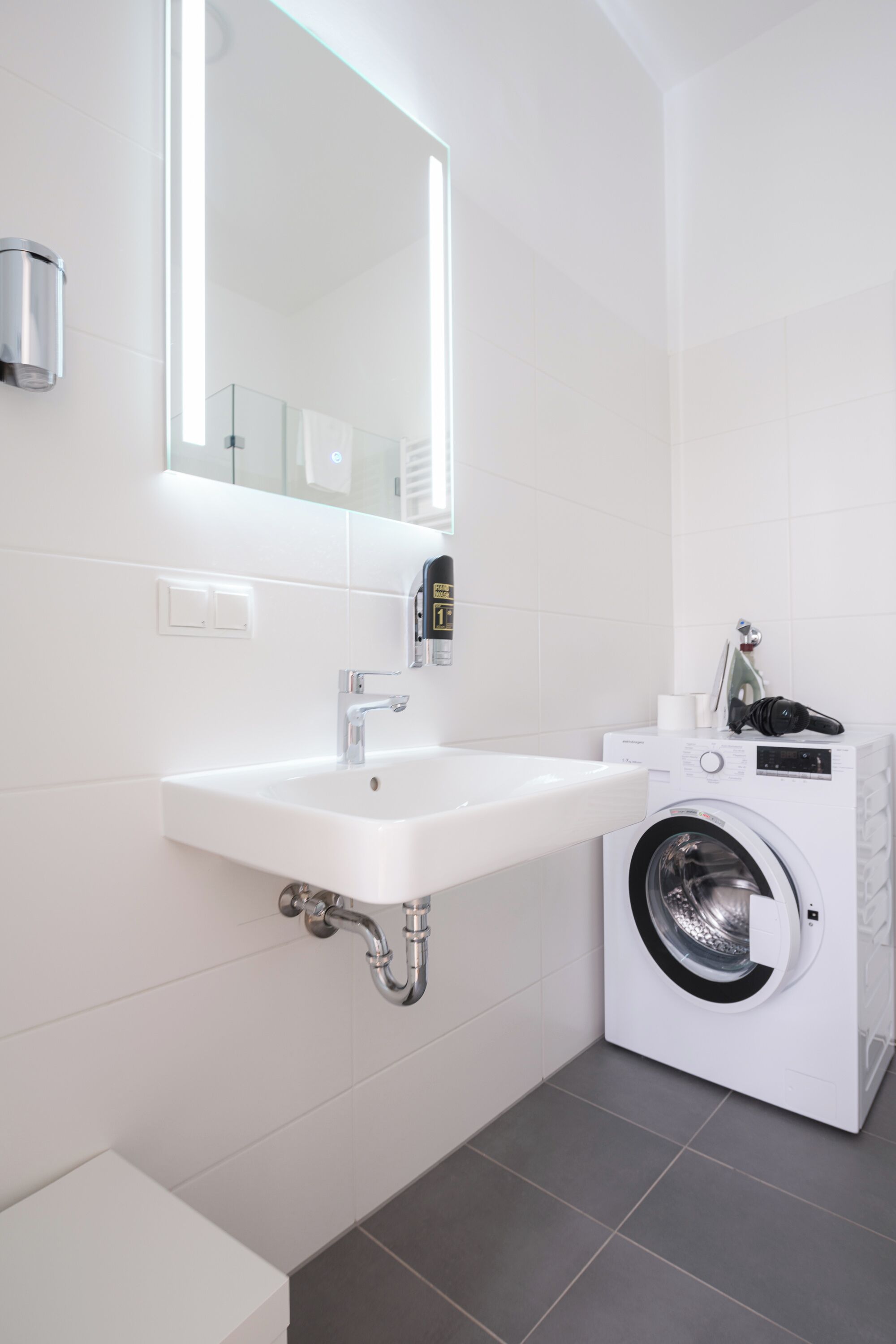 A modern bathroom with a white sink, a mirror, and a front-loading washing machine.